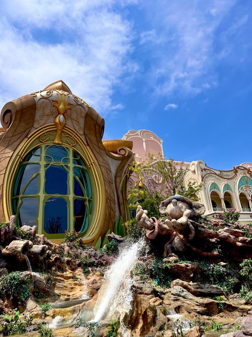 A whimsical, fairytale-like building with ornate golden details and blue-tinted windows, accompanied by a statue of a creature spouting water in the foreground.