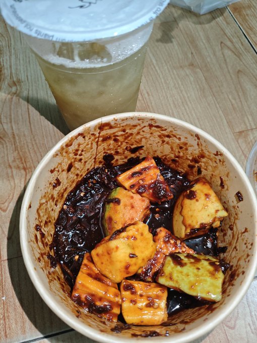 iced tea with a straw and a bowl of fruit, including mangoes and bananas, on a wooden table.