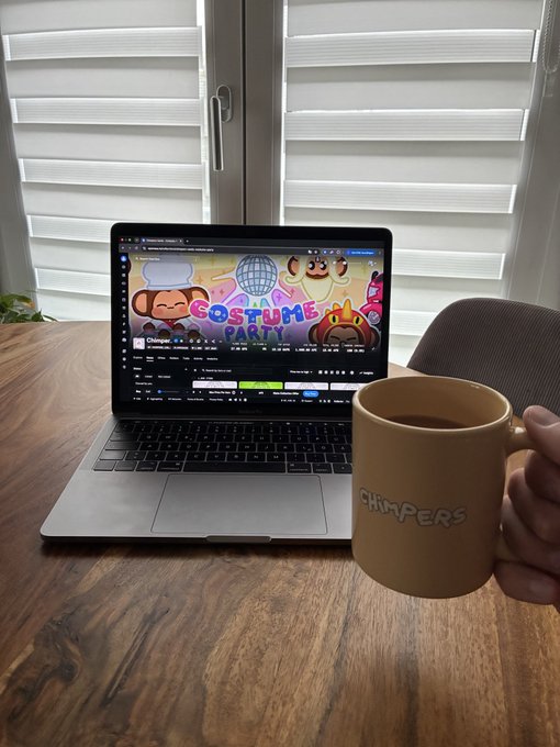 A hand holds a “Chimpers” coffee mug beside a laptop displaying ChimpersHQ’s “Costume Party” page. It matches the post’s “New day = new @ChimpersHQ Card of the Day” theme.