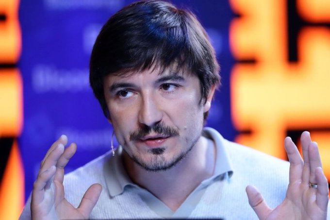 Vlad Tenev, CEO of Robinhood, speaks animatedly with both hands raised in a gesture, with a lapel microphone visible as he appears to address an audience at a conference or public event. His expressive demeanor and engaged posture reinforce the post's message of his bullish advocacy for tokenization and his push for the U.S. to embrace tokenized stocks.