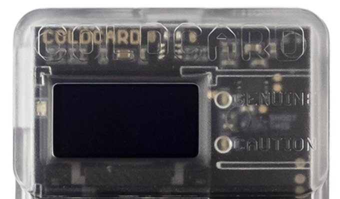 A close-up of a Coldcard Mk4 hardware crypto wallet with "GENUINE" and "CAUTION" markings visible on the transparent casing.