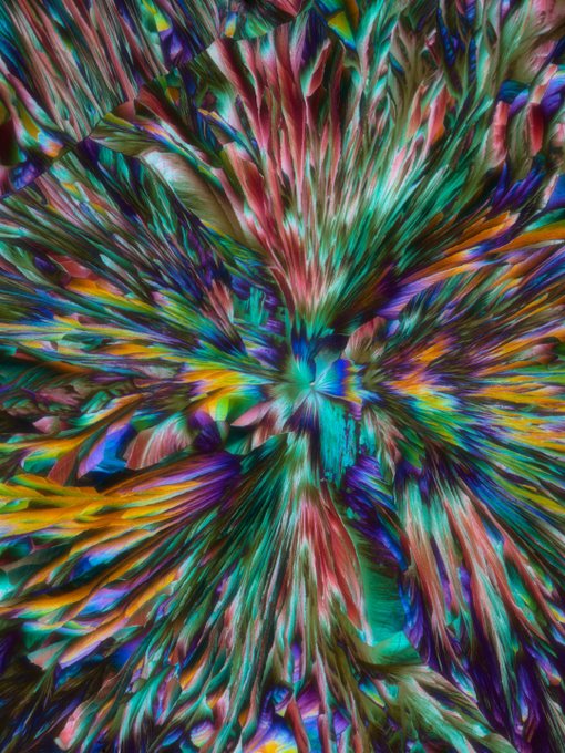 An abstract, psychedelic digital artwork featuring vibrant multicolored streaks radiating outward from a central cyan point in a starburst pattern.
