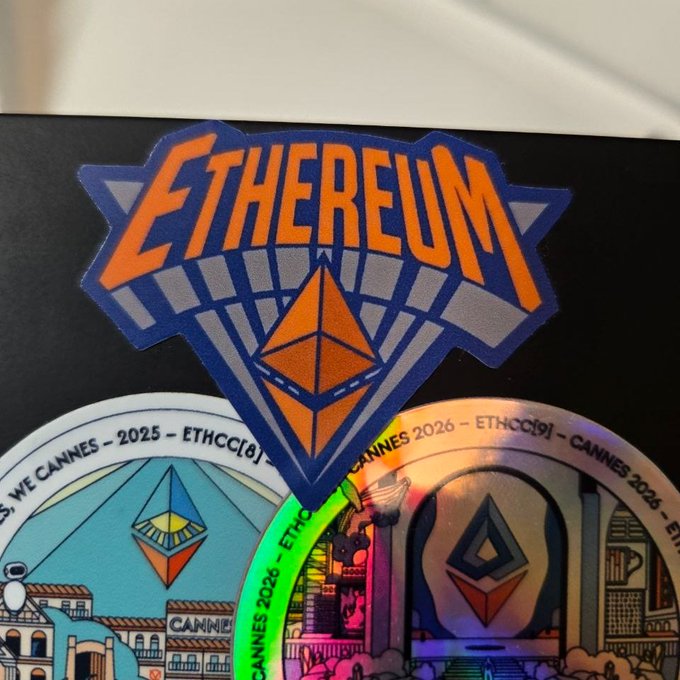 The image features a sticker with an illustration of a city skyline and the words "ETHEREUM" written above it, along with the year "2025". The sticker also includes a small triangle shape that resembles a building or tower. In the background, there is another smaller sticker featuring a cityscape as well. The text in the image reads: "NYC Ethereum meetup tomorrow Unfortunately I can't make it, but I want one of these stickers so badly", and it ends with an exclamation mark.

The main focus of the image is on the "ETHEREUM" sticker, which is prominently displayed at the top center of the frame. The city skyline sticker is located in the bottom right corner of the image.