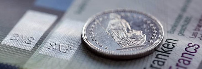 A close-up macro photograph of a Swiss franc coin resting on Swiss banknotes, with 'Franken' and 'Francs' partially visible.