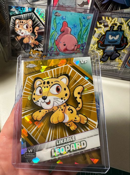 A hand holds a shiny gold "LIKABLE LEOPARD" First Chrome VF trading card in front of other animal and robot-themed cards.