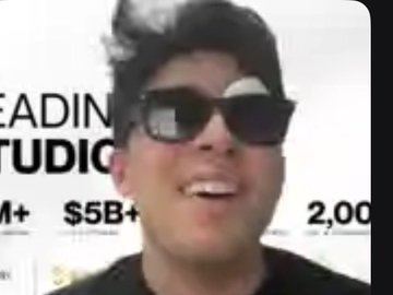 A man wearing sunglasses smiling in front of a partially visible 'LEADING STUDIO' sign with text showing '$5B+' and '2,00'.