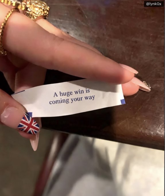A hand with decorated nails featuring a Union Jack design holds a fortune slip that reads 'A huge win is coming your way'.