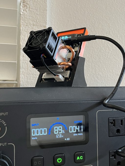 A close-up photograph of a DIY computer cooling setup featuring copper heat pipes and a fan mounted on a black stand above a portable power station displaying an 89% battery level and 0041 watts output.