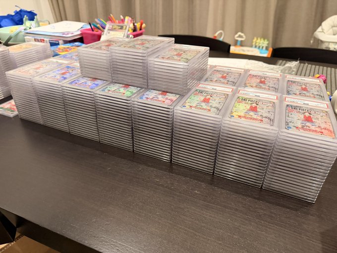 Stacks of "One Piece" trading cards (including "Replicant" and "Championship" sets) are arranged in organized rows on a dark table, with pens and supplies visible in the background, suggesting preparation for a card trading or sorting session tied to the Rutgers community.