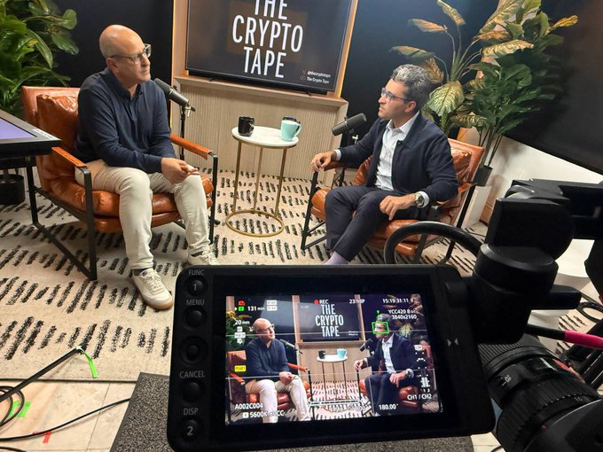 A behind-the-scenes shot of "The Crypto Tape" podcast recording featuring Joseph Chalom, CEO of Sharplink, seated across from the host with a camera and monitor visible in the foreground capturing their discussion about Ethereum's role in the future of finance.