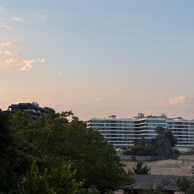 Evening sunset sky over a cityscape with a Novotel hotel and trees in the foreground.