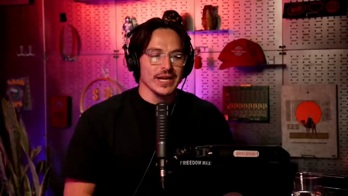 The image features a man wearing glasses, sitting behind a microphone at a desk with a computer monitor. He appears to be speaking into the microphone or giving a presentation. The background of the image includes a wall covered in various items such as posters and knick-knacks, suggesting that it is likely an office environment.

The post on Wall Street's SECRET Plan to steal your Bitcoin reads: "Opti Explains Wall Street's SECRET Plan To Steals Your Bitcoin". This text is located at the bottom of the image, indicating that this content is related to the man speaking into the microphone or giving a presentation in front of it.

The post seems to be discussing a topic related to cryptocurrency and potentially offers advice on how to protect one's digital assets from theft.