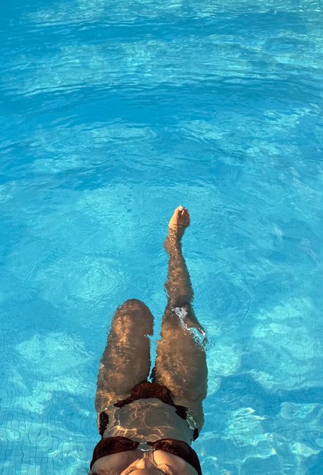 A person's legs are visible beneath the clear, bright blue water of a swimming pool.