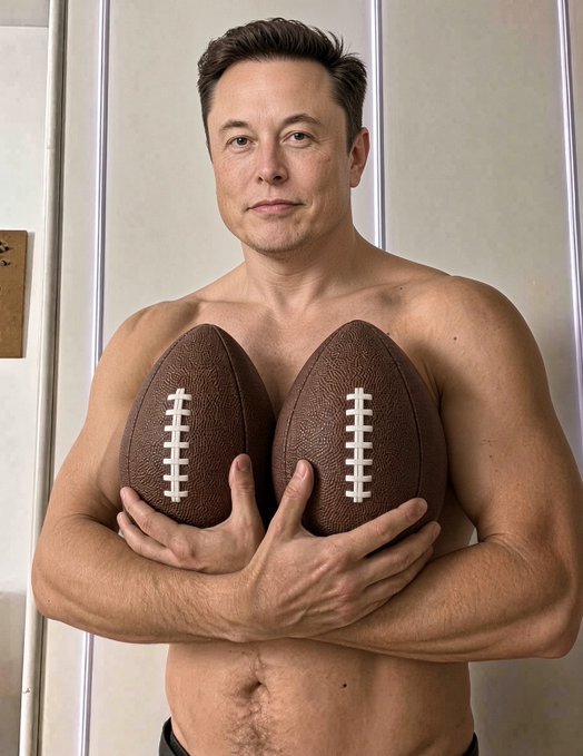 A shirtless man with a muscular build holds two footballs against his chest indoors.