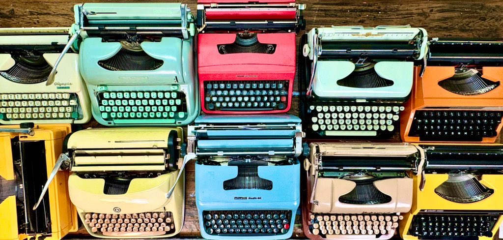 A colorful collection of vintage typewriters, including a teal Olympia, red Consul, blue Curiss, and several others in cream, orange, and yellow hues, are arranged tightly together as if displayed for sale. The image complements the poster's mention of "15 total" and "333" by visually representing a growing collector's inventory of unique typewriter models.