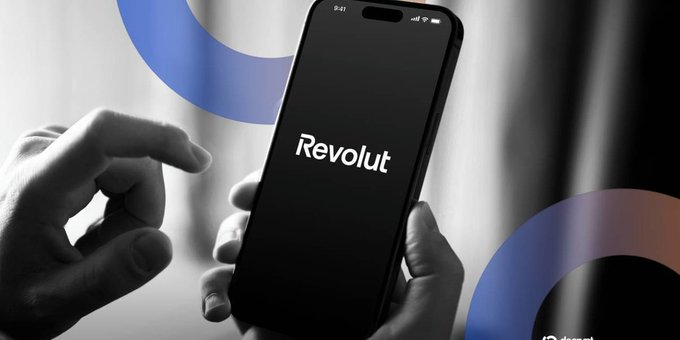 A person holding a smartphone displaying the 'Revolut' app logo on a black screen, with blue circular graphic overlays and a black and white filter on the hands and background.