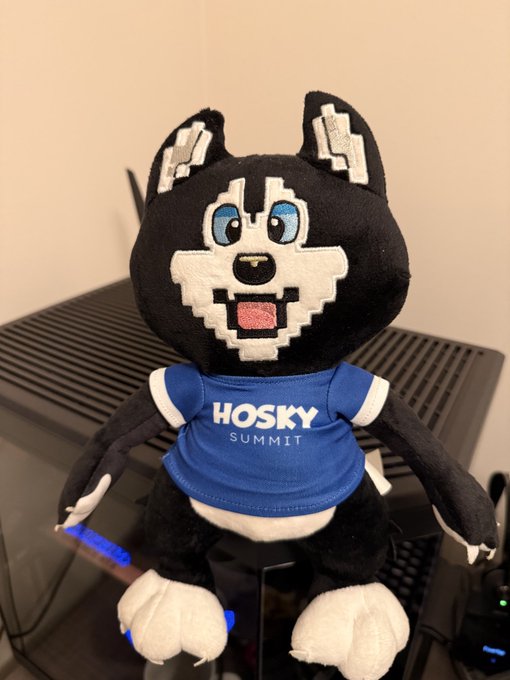 A Husky mascot plush toy wearing a blue 'HOSKY SUMMIT' shirt, sitting on what appears to be a computer tower.