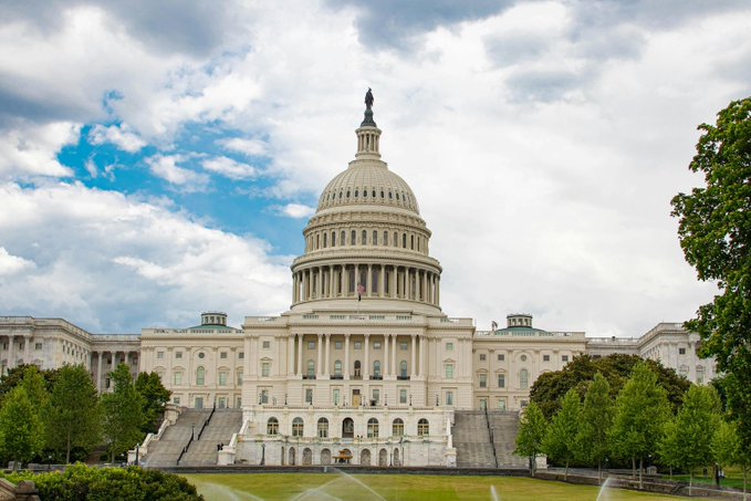 The image shows the U.S. Capitol Building in Washington, D.C., with its iconic white dome and surrounding grounds under a partly cloudy sky. This relates to the accompanying post, as the Capitol is where the U.S. Senate convenes to consider legislation like the CLARITY Act, the bill discussed in the post regarding cryptocurrency provisions.