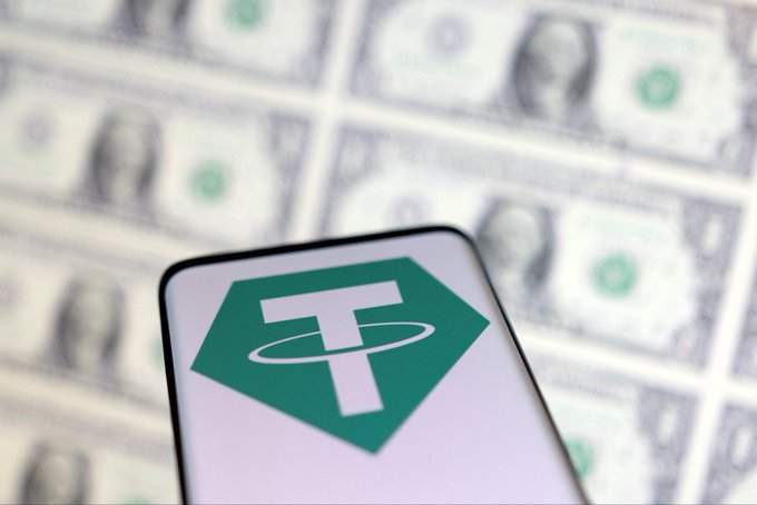 The Tether (USDT) logo is displayed on a smartphone screen, set against a backdrop of US dollar bills. This visual ties directly to the news of Tether receiving its first unqualified audit from KPMG, highlighting the connection between the stablecoin and the traditional fiat currency it is pegged to.