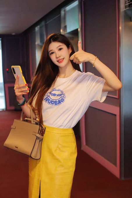 A young woman smiles and gives a thumbs-up while holding her phone, wearing a white "NUOBIO" t-shirt and yellow skirt, posing as a cheerful "gm" greeting to accompany HTX's impressive 24-hour trading stats.