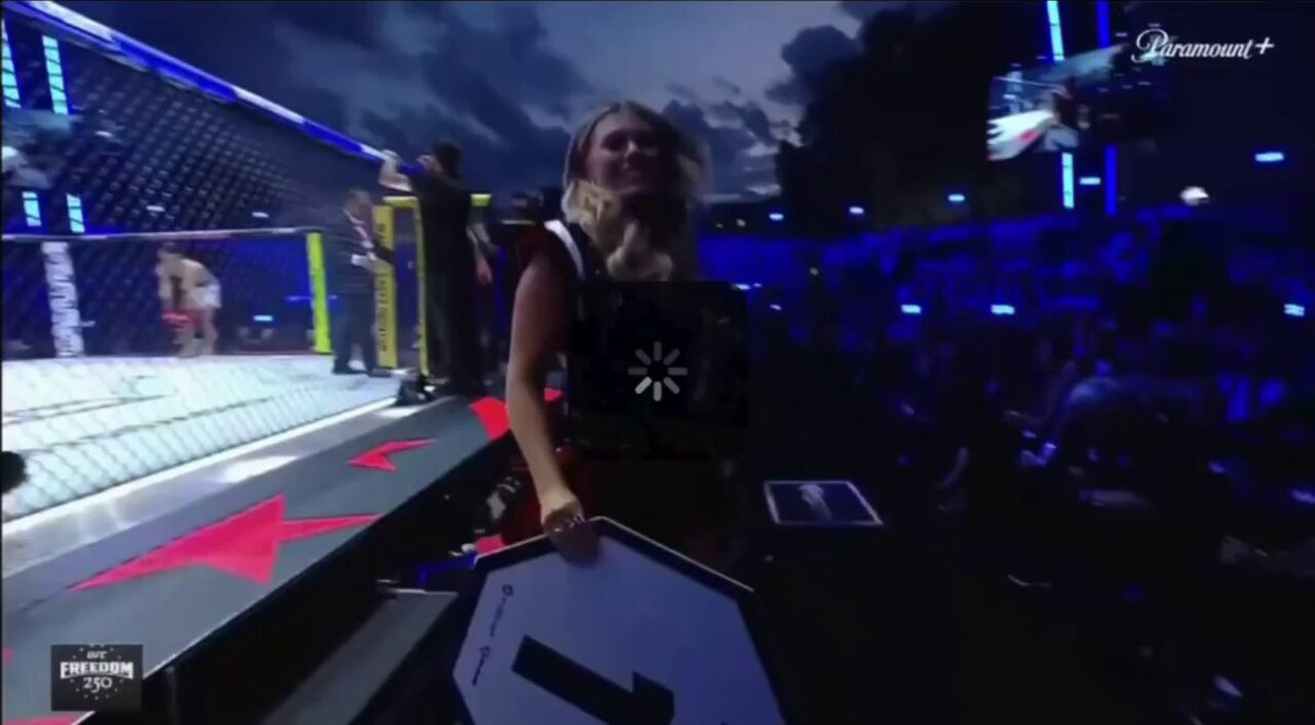 This image captures an MMA fighter walking across a stage with her opponent sitting on a chair behind her, possibly during a UFC fight-night competition. In addition to them, there are several other people visible in the scene, though they do not seem to be directly involved in the main action. The image is set against a blue sky background, creating an interesting contrast between the fighter and her opponent.

The primary focus of this image is on the fighter as she walks by her opponent, who appears to have taken the opportunity during the fight-night event at the UFC headquarters to grab some cash for her, known as the UFC Freedom bonus pool. The post seems to be about a UFC fight night that took place recently and possibly involves an analysis of the fighters' performance or the overall events surrounding it.