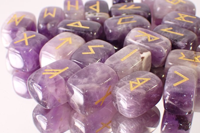 A collection of polished purple amethyst rune stones engraved with gold Elder Futhark symbols, featured as the prize in a giveaway campaign where two winners will receive the rune stone set by following and reposting the post.
