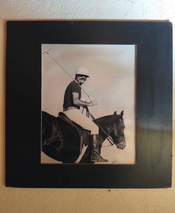 A framed black-and-white photograph of a man wearing a helmet and sunglasses, riding a horse while holding a long polo mallet.