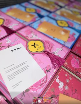 A display of pink and orange Mid-Autumn Festival gift boxes from XME, featuring decorative tassels and floral packaging, sits alongside an information card with the "xme" logo and participation details.