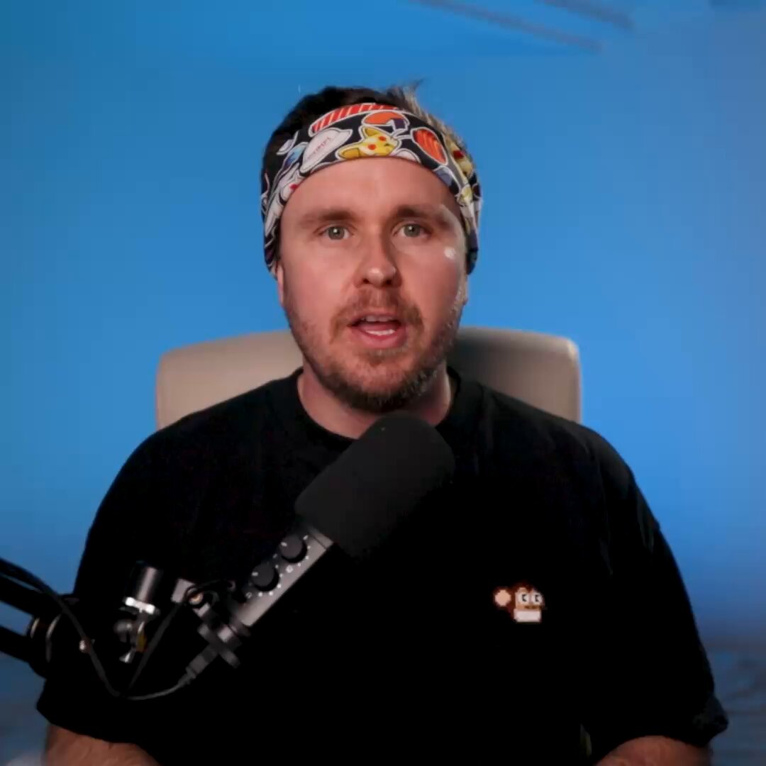The image features a man wearing a black t-shirt with a monkey design on it, sitting behind a microphone. The background of the image is blue, which contrasts with the man's attire. There are no other objects or people visible in the photo. The caption at the bottom of the image reads "In case you missed it. Updates on brand, community, NFTs".