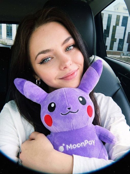 A young woman in a car holding a purple Pikachu plush toy wearing a 'MoonPay' shirt.