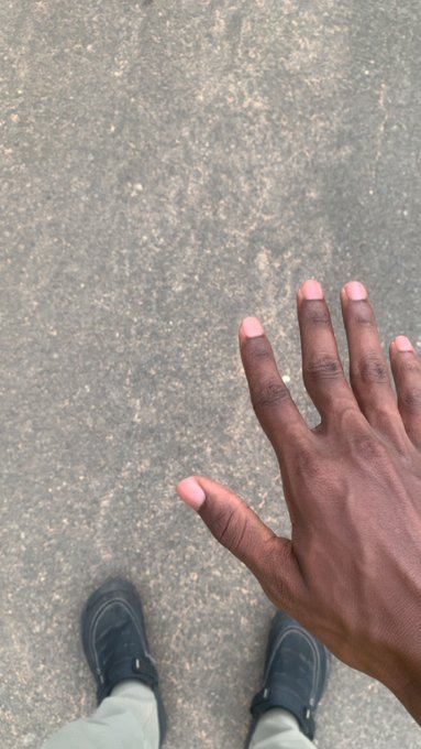 A first-person view looking down at a hand held out over an asphalt surface, with the person's feet and black sneakers visible at the bottom of the frame.