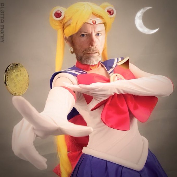 A man dressed as Sailor Moon with yellow pigtail wig, red bow, and white gloves, holding out his hand with a Bitcoin coin superimposed, captioned 'ALATTA MONEY'.