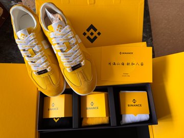 A pair of yellow and white sneakers displayed with a Binance gift box containing socks and cards, with Binance branding visible on the packaging.