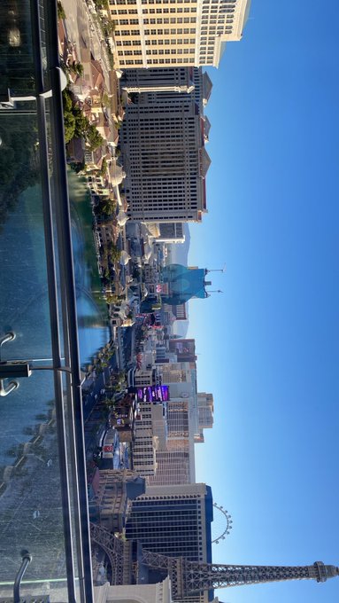 The image (rotated 90°) shows a daytime view of the Las Vegas Strip, featuring recognizable landmarks like the Paris Las Vegas Eiffel Tower replica and the High Roller Ferris wheel under a clear blue sky. The bright daylight contrasts with the post's "Good morning or good night?" greeting, suggesting a morning scene in the entertainment capital of the world.
