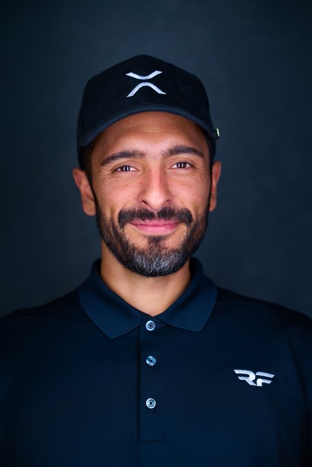 A smiling man with a beard wears a black cap featuring the XRP logo and a black polo shirt with an "RF" emblem, visually representing the personal branding of a crypto entrepreneur reflecting on his post-Linqto achievements.