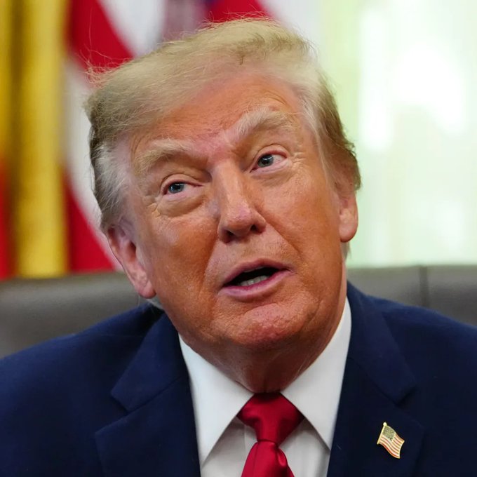 A man in a dark blue suit, red tie, and American flag lapel pin speaks in an official setting with a flag visible in the background. The image accompanies reports of the US preparing to seize $1 billion in crypto assets to economically isolate Iran.