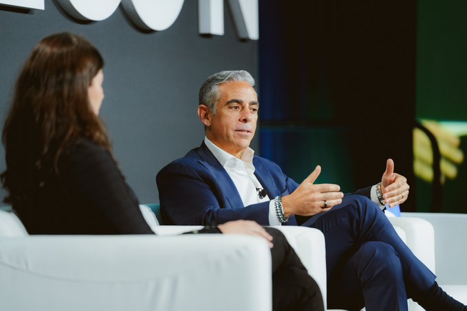 A man in a navy suit gestures animatedly while speaking on stage at Stablecon in DC, seated across from a woman in dark attire during a panel discussion about instant, stablecoin-settled money movement.