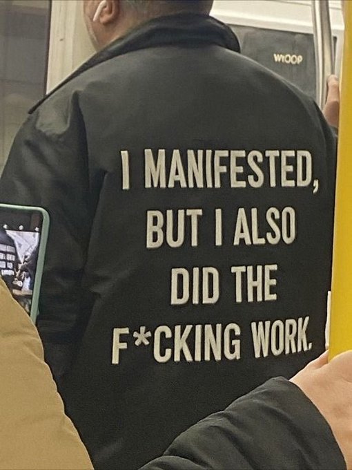 The back of a person's black jacket displays the text "I MANIFESTED, BUT I ALSO DID THE F*CKING WORK."