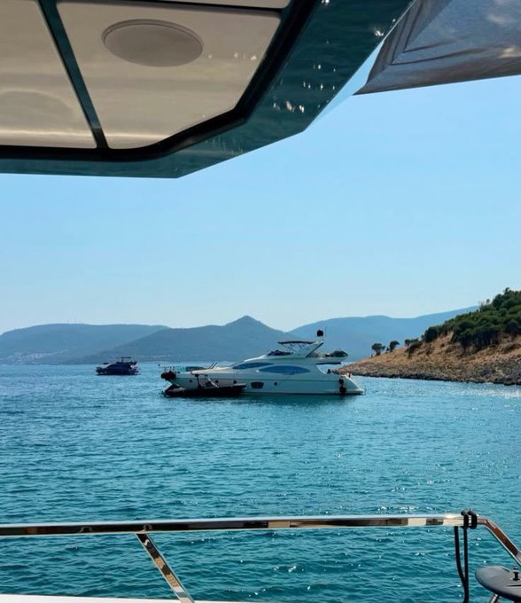 A luxury yacht anchored in clear turquoise waters with mountains in the background, viewed from the deck of another boat. The post's confident "let's make money" sentiment pairs with the aspirational lifestyle of leisurely yachting on a sunny day.