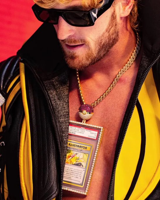 A man with sunglasses and a beard wearing a black and yellow jacket, displaying a large pendant with a Pokemon card labeled 'ILLUSTRATOR' encased in diamonds.