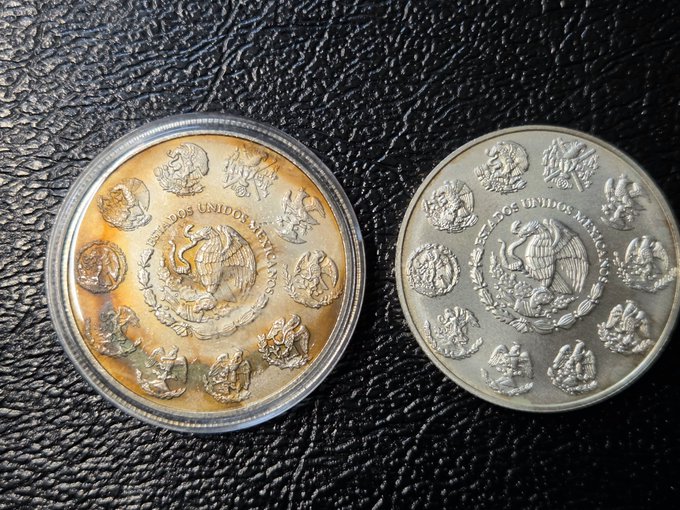Two Mexican silver coins, one with golden toning in a capsule and one unencapsulated, both showing the national eagle emblem and 'ESTADOS UNIDOS MEXICANOS' text on their reverse sides.