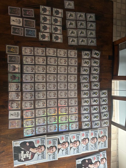 A wooden floor covered with a large collection of trading cards, video game cases, and multiple copies of a magazine titled "You Can Enter Your World" featuring two men on the cover.