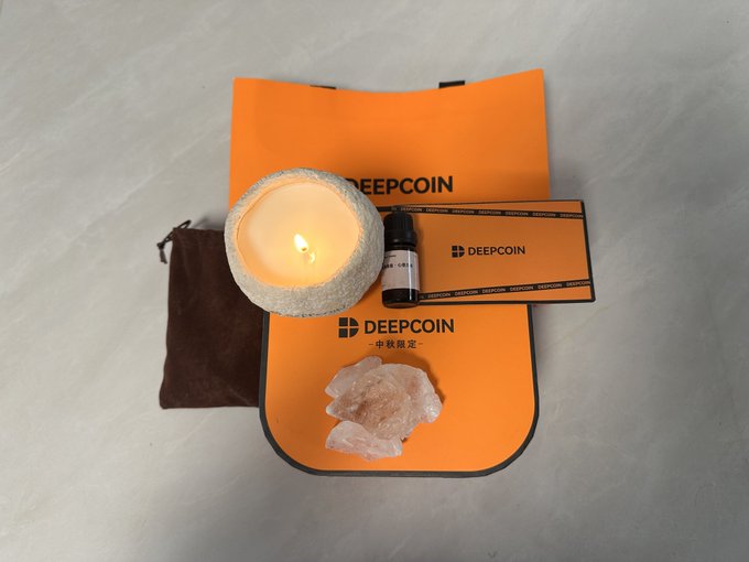 A flat lay of DEEPCOIN branded products including a lit candle, a small bottle, a brown pouch, a rose quartz-like crystal, and orange packaging cards.