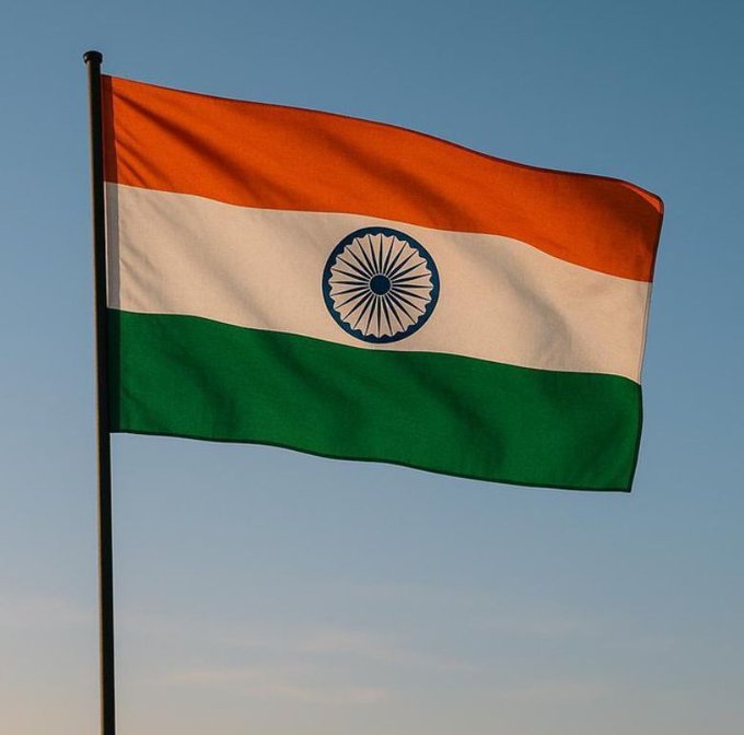 The flag of India, featuring horizontal stripes of saffron, white, and green with the blue Ashoka Chakra in the center, waves against a clear blue sky.