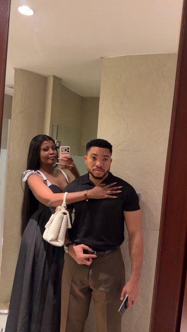 A well-dressed couple poses for a mirror selfie in an upscale setting, with the woman holding a phone to capture the moment while holding a white handbag, and the man in a black polo shirt looking confidently at the camera. The polished, affluent appearance of the pair visually reinforces the post's theme of crypto investment success, suggesting the lifestyle rewards that come from strategic engagement in tech and related industries.