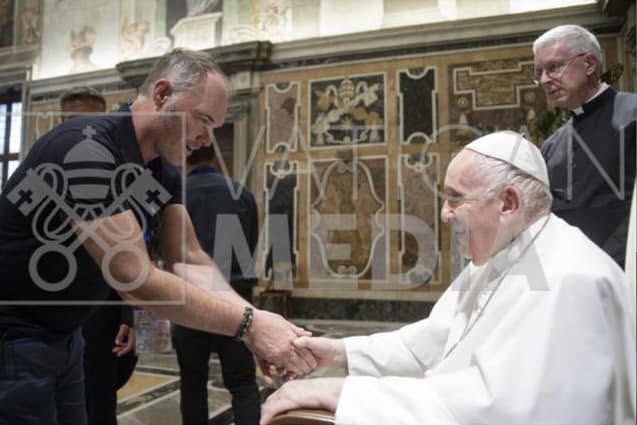 Pope Francis shakes hands with a smiling man in a dark shirt, accompanied by a clergyman in the background, in an ornate Vatican setting. The image, watermarked "Vatican Media," appears to depict a public papal audience that the post sarcastically references in connection to the men allegedly involved in a $250 million theft.