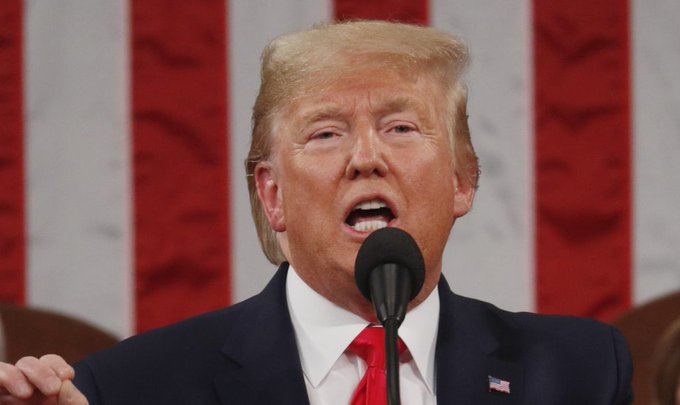 President Donald Trump is depicted in a portrait-style image with the American flag in the background. He is captured in mid-speech, with a microphone positioned before him, indicative of a formal address or speech. This scene visually corresponds to the claim that he is discussing economic policies, such as the potential removal of taxes on Bitcoin and crypto transactions, which could significantly affect the adoption of cryptocurrencies in the U.S. The image does not provide direct evidence of the content of his speech but shows what could be a discussion of economic policy given his role as President and the context of the accompanying statement on cryptocurrency taxation.