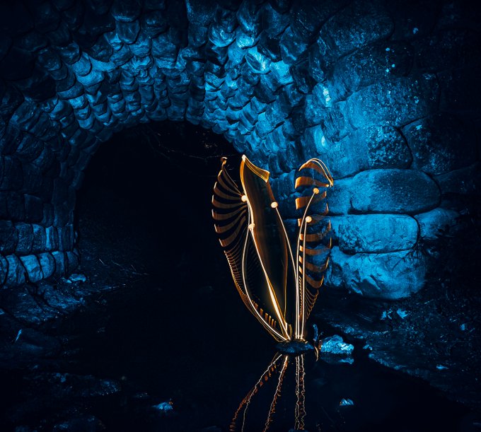 The image features a large stone archway with a bird-like structure inside, which appears to be made of metal or glass. The photo has been taken using the light painting technique, as indicated by the caption "0.25 $ETH". This method involves shining a light through a transparent medium and manipulating the light waves to create an image on a photosensitive surface. In this case, it seems that someone used a light source to paint the bird-like structure inside the archway with a reflection of the surrounding environment. The photo is taken from a low angle, which emphasizes the size and shape of the archway as well as the bird-like structure within it.