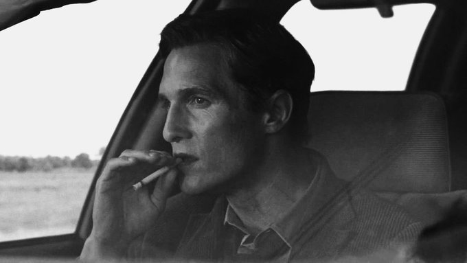 In this image, a man dressed in business clothes sits inside a car with his hand on his chin while smoking a cigarette. The black and white color scheme gives it a classic or vintage feel. A caption related to the image suggests that spotting the market bottom can be done by wiping out long teams using leverage, which seems applicable to this scenario because it appears to involve a man in business attire making an important decision based on financial information within the context of the market.