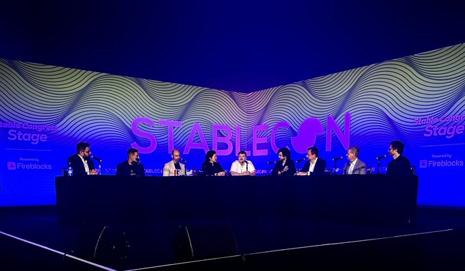A panel discussion at 'STABLECON' with multiple speakers seated at a long table in front of a large stage screen.